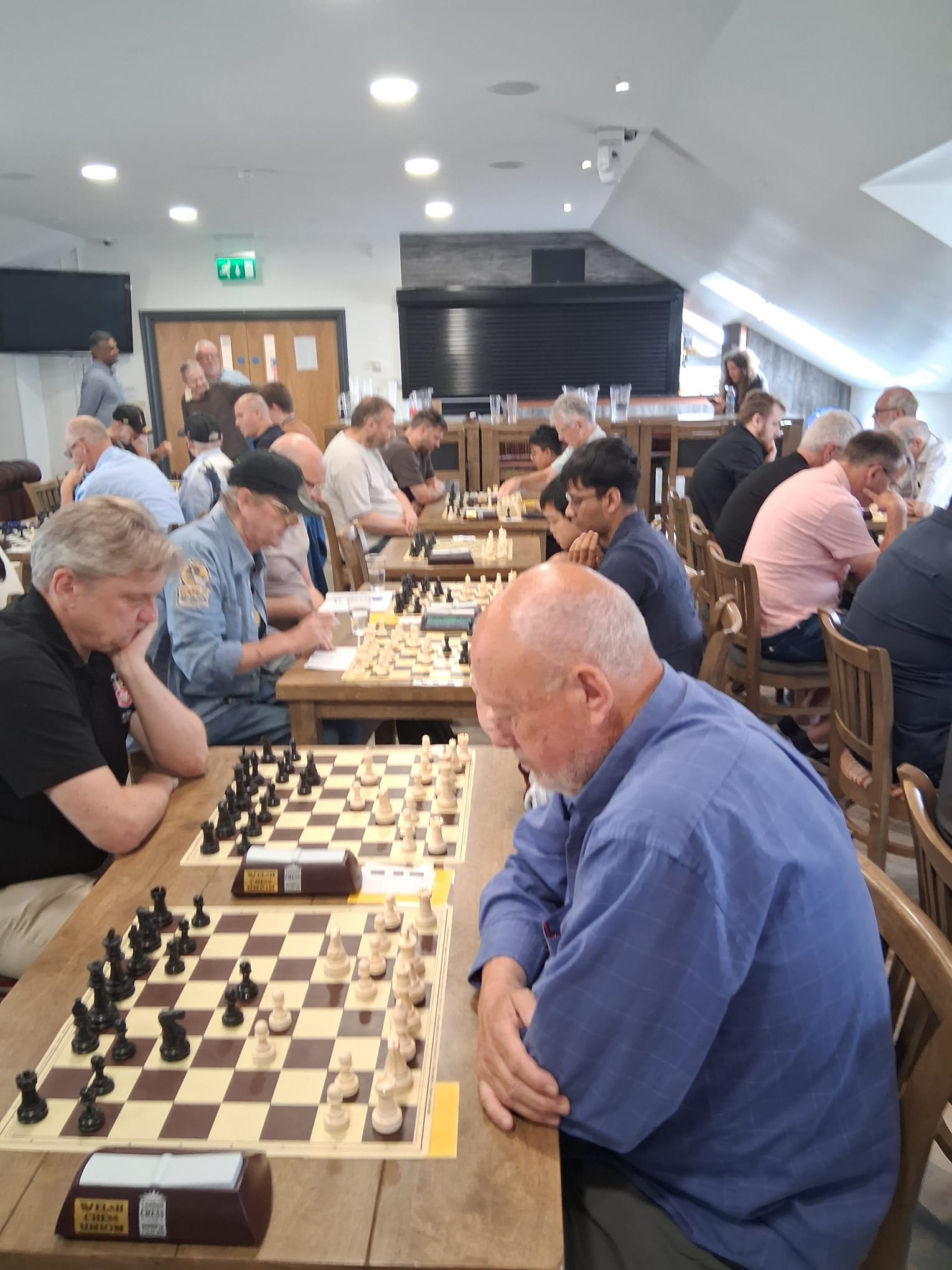A crowded room of chess players of all ages, mid-game across rows of boards